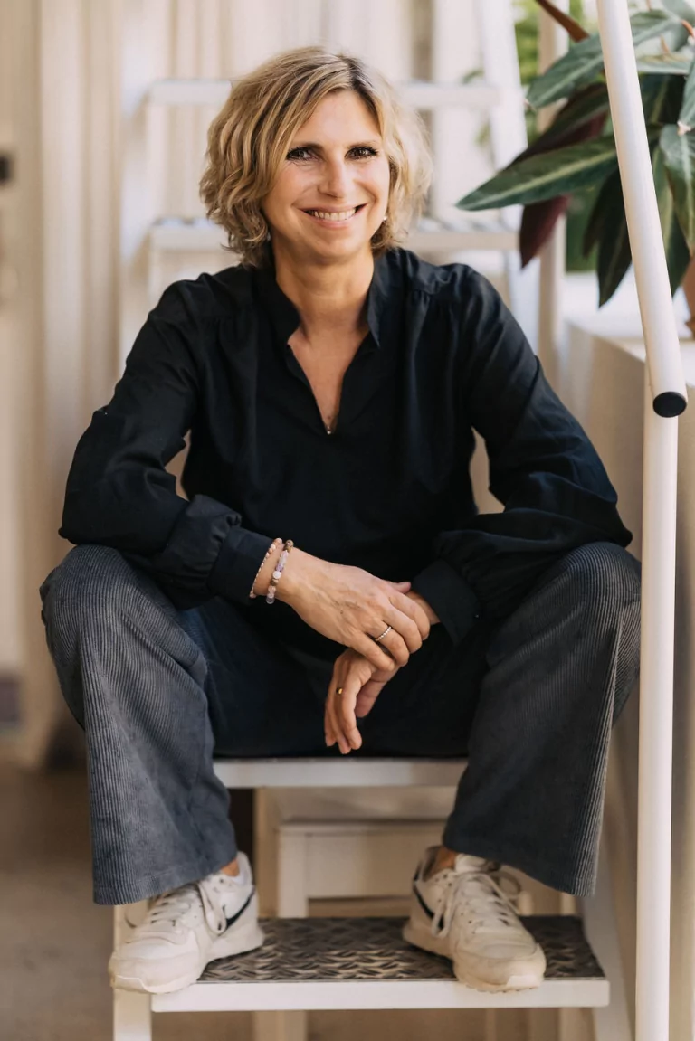 Portrait von Achtsamkeitstrainerin Alexandra Wittek. Alex Wittek sitzt bequem auf einer Treppe und lacht in die Kamera.